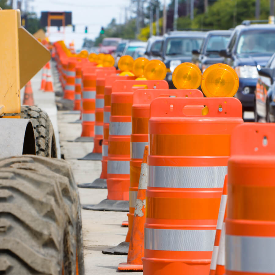 Line of orange construction traffic barrels with warning lights on a busy road during roadwork